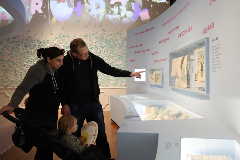 Ngày 7/4 tại Bảo tàng Dân gian Quốc gia ở quận Jungno, Seoul, một gia đình người nước ngoài tham quan triển lãm đặc biệt 'Sinh con, niềm vui chung của mọi nhà' đang tìm hiểu về hình dáng xưa và nay của địu em bé. Từ xưa ở Hàn Quốc đã có truyền thống 'eobuba' - cõng trẻ trên lưng bằng 'podaegi', một loại địu làm từ vải chần bông có dây dài. Trong khi phương Tây thường ẵm con phía trước, cách thức truyền thống của Hàn Quốc có đặc điểm riêng là giúp tăng sự gắn kết giữa mẹ và con. (Ảnh: Park Daejin / Korea.net)