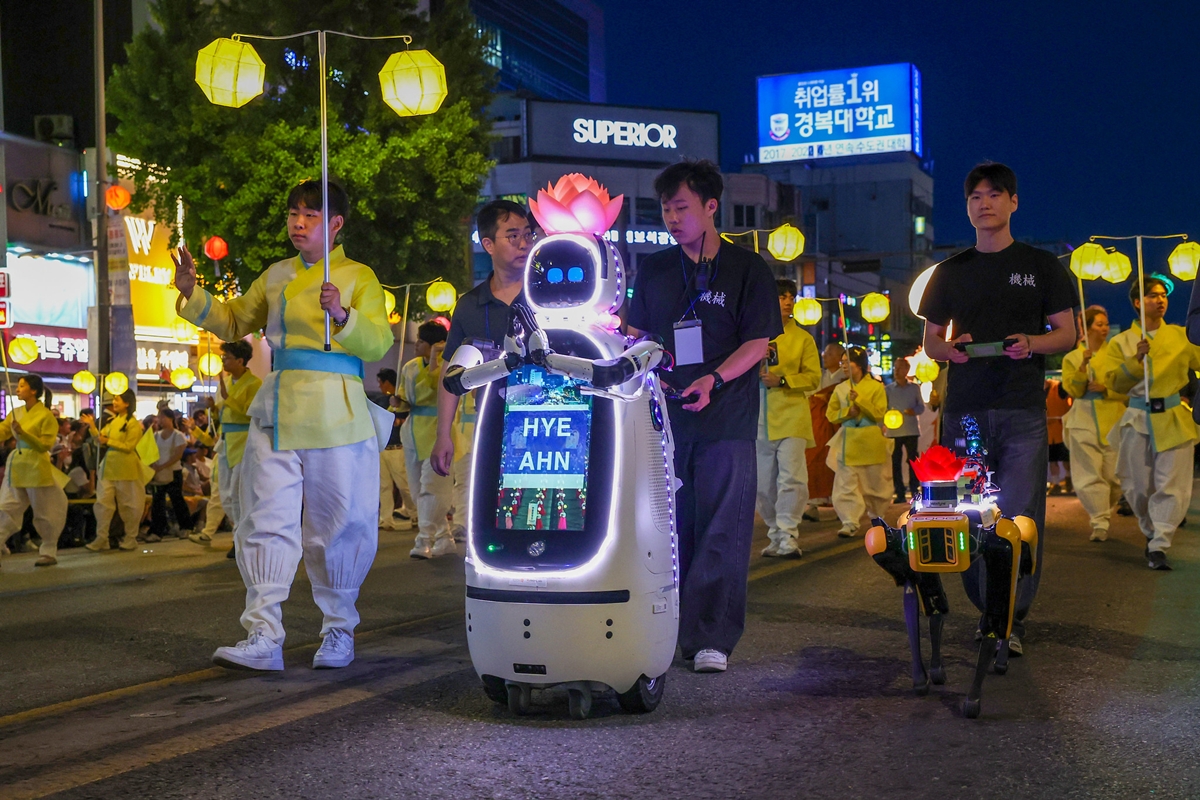 Robot nh&agrave; sư AI Hyean (tr&aacute;i) v&agrave; robot bốn ch&acirc;n đa cảm biến Googi d&ugrave;ng cho tuần tra v&agrave; an to&agrave;n dẫn đầu đo&agrave;n diễu h&agrave;nh đ&egrave;n lồng của Đại học Dongguk&nbsp;tại lễ hội Yeondeunghoe diễn ra ở khu vực Jongno, Seoul trước thềm lễ Phật đản ng&agrave;y 16/5. (Ảnh: Lee Jeong Woo / Korea.net)