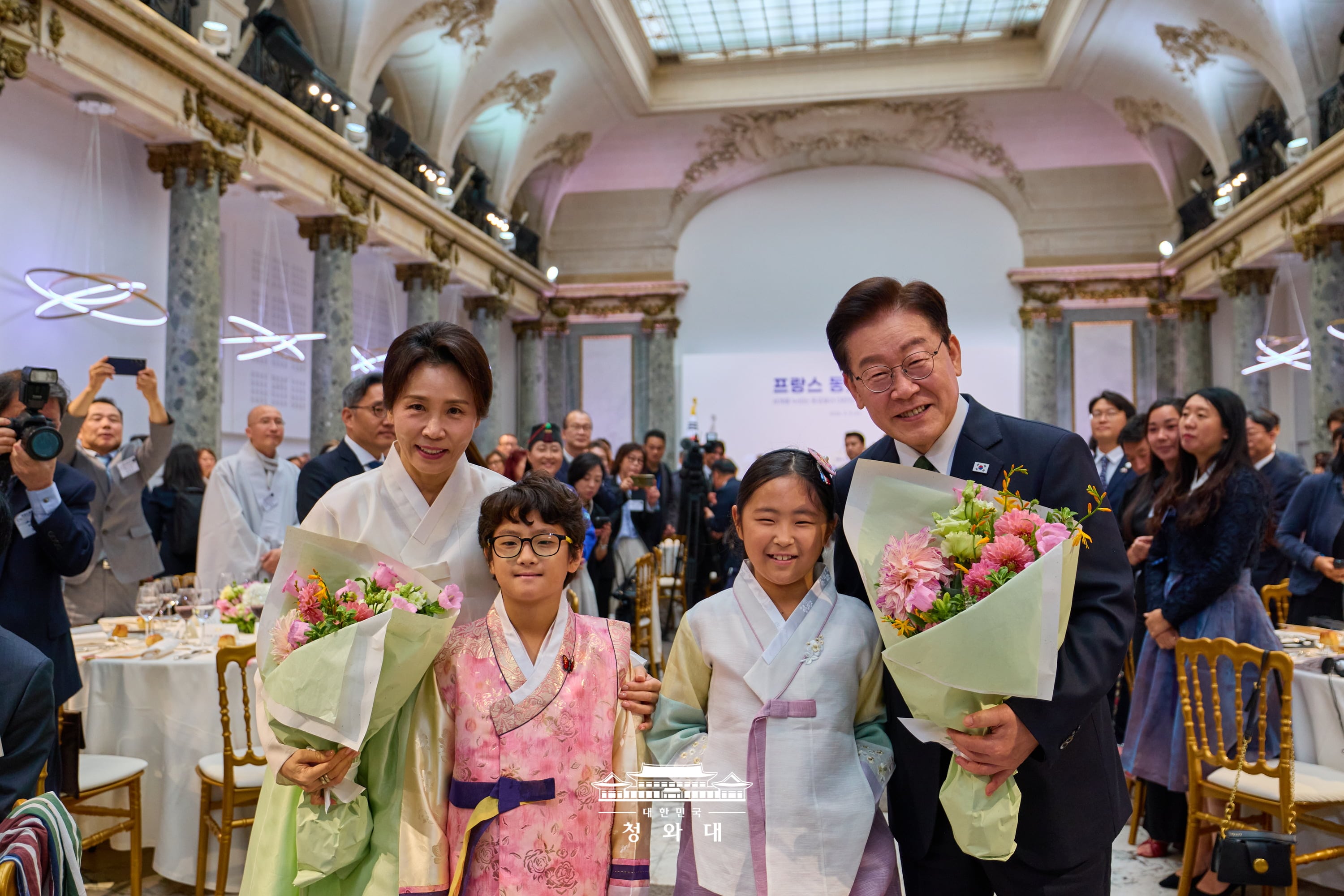 Tổng thống Lee Jae Myung v&agrave; Đệ nhất phu nh&acirc;n Kim Hye Kyung chụp ảnh lưu niệm với b&oacute; hoa được c&aacute;c em thiếu nhi tặng tại buổi gặp mặt ăn trưa với cộng đồng người H&agrave;n Quốc, diễn ra tại Pavillon Cambon ở Paris, Ph&aacute;p, ng&agrave;y 9/9 (giờ địa phương). (Ảnh: Nh&agrave; Xanh)
