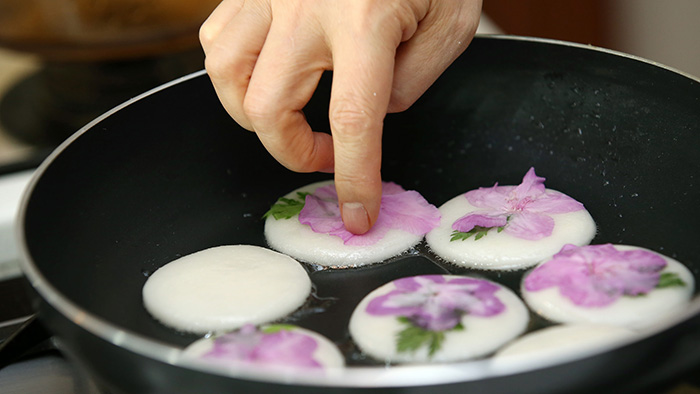 Khi một mặt bánh đã chín thì lật bánh lại, sau đó đặt cánh hoa đỗ quyên lên trên. Lưu ý điều chỉnh lửa, để ở lửa nhỏ cho mặt bánh trơn đẹp.