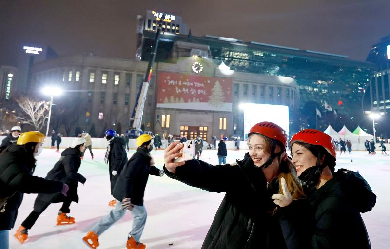 Du khách nước ngoài đang chụp ảnh kỉ niệm tại sân trượt băng Seoul Plaza, Jongno-gu, Seoul sau khi được mở lại vào ngày 21/12. (Ảnh: Yonhap News)