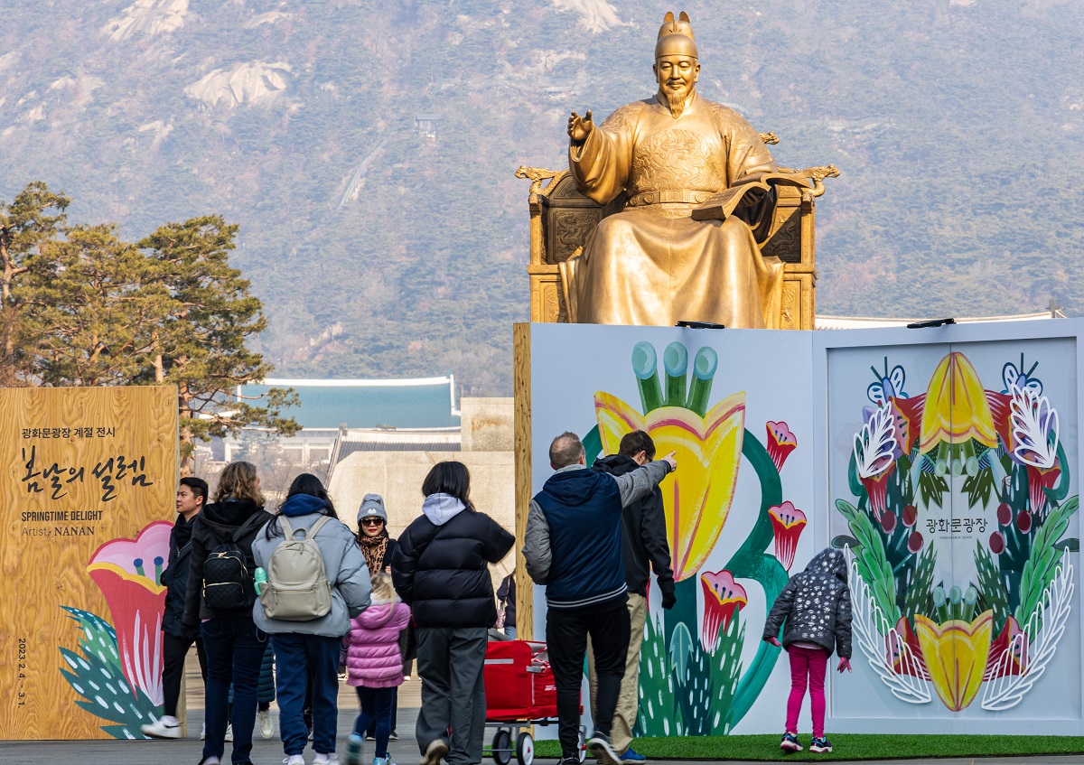 Ngày 17/02, các du khách nước ngoài đang xem Photo Wall tranh hoa được lắp đặt ở quảng trường Gwanghwamun, Jongno-gu (Seoul), như một phần của triển lãm theo mùa mang tên “Sự rung động ngày Xuân”. (Ảnh: Yonhap News)